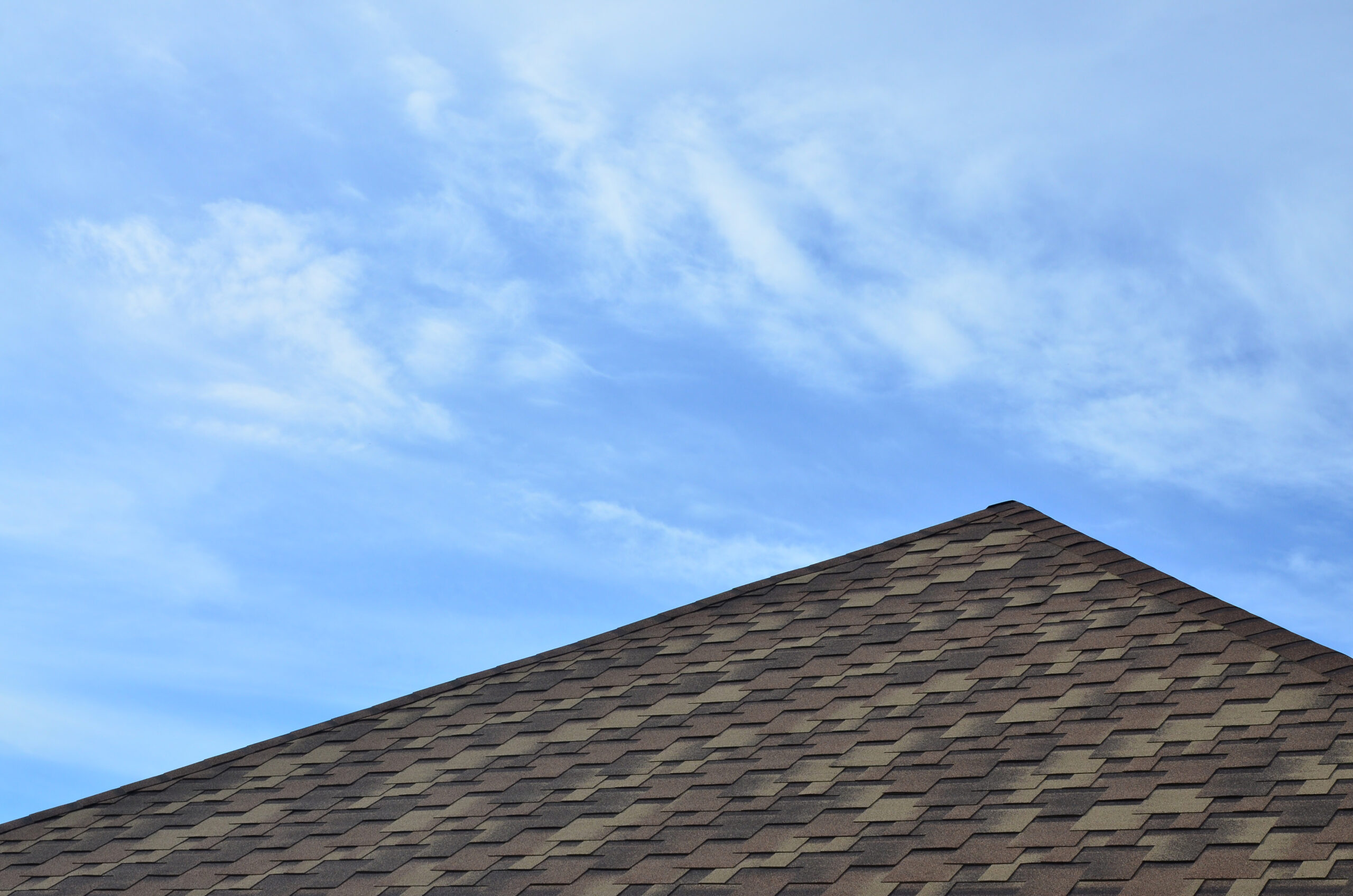 The roof of a residential house, covered with a modern flat bituminous waterproof coating under a blue cloudy sky. The concept of high-quality roofing with bituminous coating