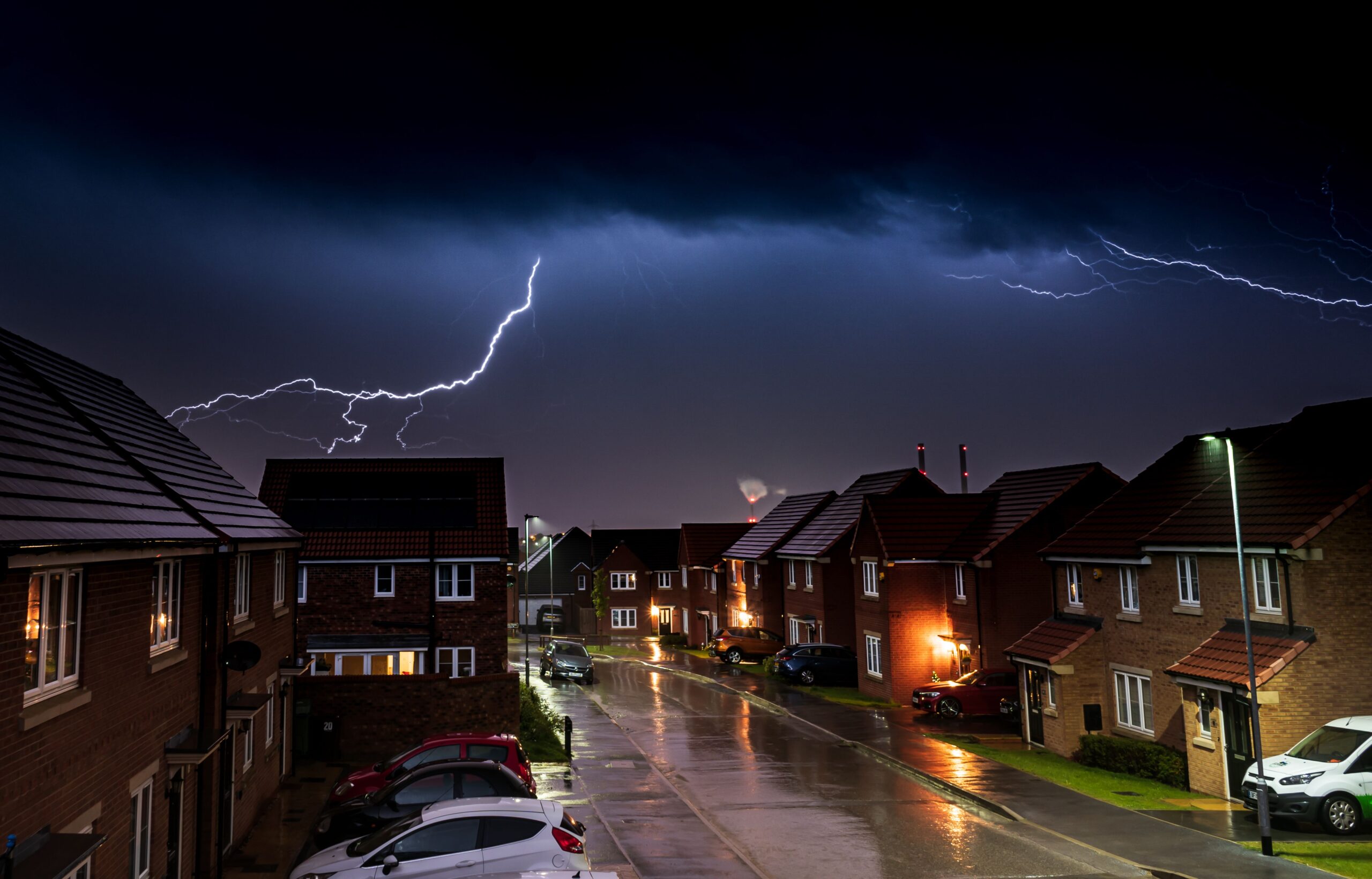 Vivid lightning strike illuminating an urban landscape at night, featuring houses and cars