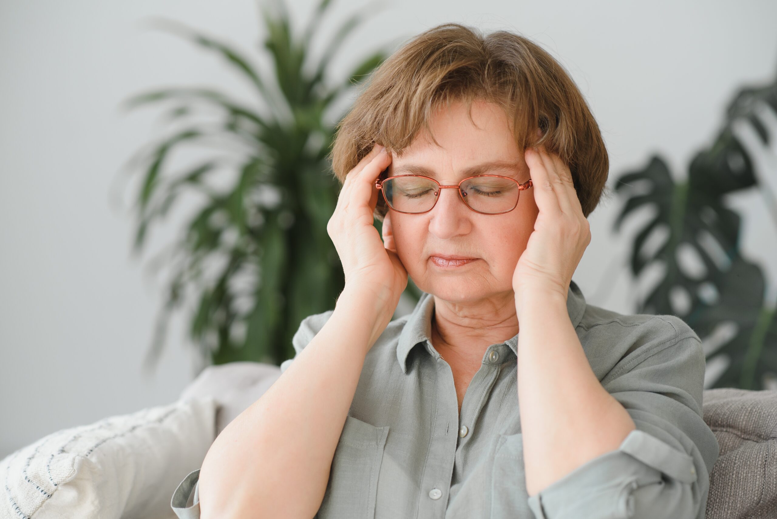 Elderly senior woman massaging her temples to reduce her headache.